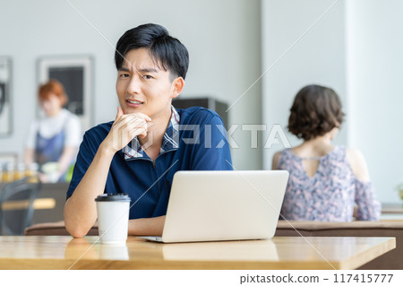 Young man looking at a laptop in a cafe Young man looking at a laptop in a cafe 117415777