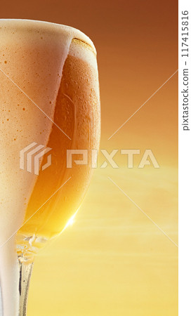 Close-up of glass with golden drink, covered in droplets against backdrop of warm golden light. Close-up of glass with golden drink, covered in droplets against backdrop of warm golden light. 117415816