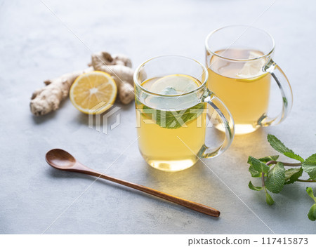 Two glasses of tea with fresh lemon, mint and ginger on a light background with morning light. 117415873