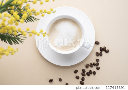 A spring bouquet with yellow mimosa flowers over a cup of coffee  cappuccino on a beige table  117415891