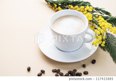 A spring bouquet with yellow mimosa flowers and a cup of coffee cappuccino on a beige table A spring bouquet with yellow mimosa flowers and a cup of coffee cappuccino on a beige table 117415893