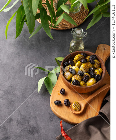 A set of green and black dried olives in bowl on a wooden cutting board on a dark background A set of green and black dried olives in bowl on a wooden cutting board on a dark background 117416113