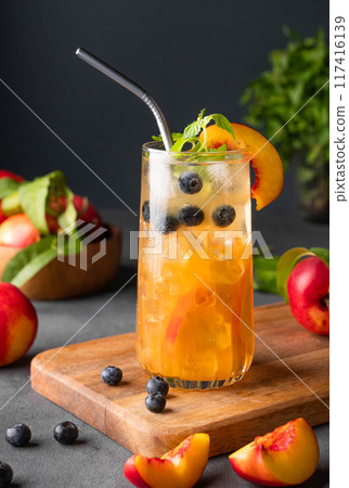 Peach tea with ice, mint and blueberry on tall glass. Vegan homemade cold healthy drink Peach tea with ice, mint and blueberry on tall glass. Vegan homemade cold healthy drink 117416139