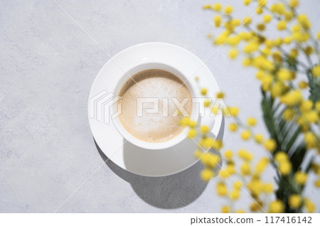 A spring bouquet with yellow mimosa flowers over a cup of coffee  cappuccino on a light background  117416142