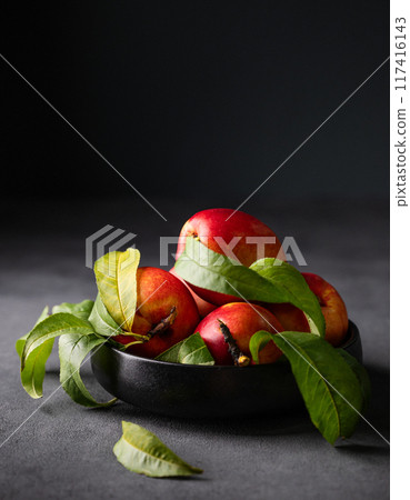 Juicy and sweet nectarines in a black bowl on a dark background.  117416143