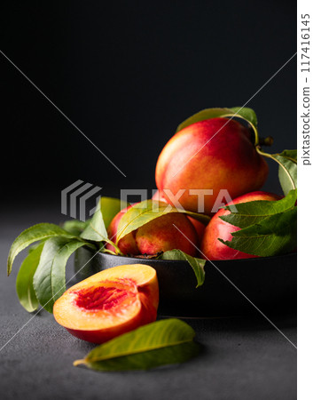 Juicy and sweet nectarines in a black bowl on a dark background close up.  Juicy and sweet nectarines in a black bowl on a dark background close up.  117416145