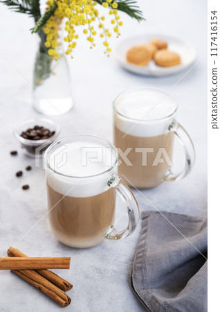 Two cappuccino or latte with milk foam in glasses on a light blue background with coffee beans 117416154