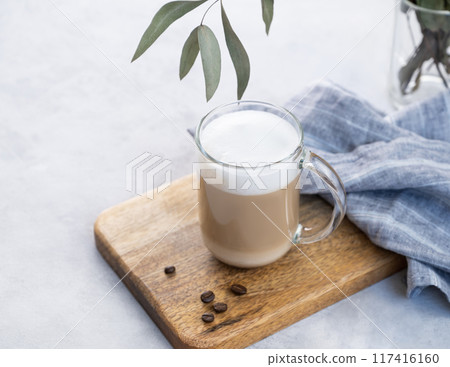 Cappuccino or latte with milk foam in glass on a wooden plate on a light blue background with coffee Cappuccino or latte with milk foam in glass on a wooden plate on a light blue background with coffee 117416160