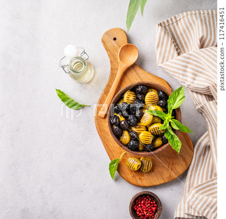 A set of green and black dried olives in wooden  bowl on a light background with olive oil and basil 117416451