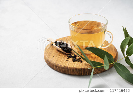 Fragrant herbal tea in a glass cup on a cutting board on a white background with eucalyptus branches 117416453