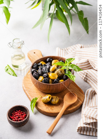 A set of green and black dried olives in wooden  bowl on a light background with olive oil and basil 117416454