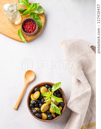A set of green and black dried olives in wooden  bowl on a light background with olive oil and basil 117416457