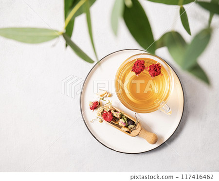 Fragrant herbal tea with pomegranate flowers in a glass cup on a plate on a white background 117416462