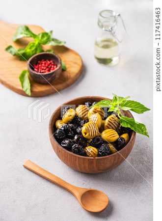 A set of green and black dried olives in wooden bowl on a light background with olive oil and basil A set of green and black dried olives in wooden bowl on a light background with olive oil and basil 117416463