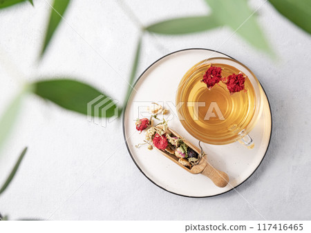 Herbal tea with pomegranate flowers in a glass cup on a plate on a white background with eucalyptus Herbal tea with pomegranate flowers in a glass cup on a plate on a white background with eucalyptus 117416465