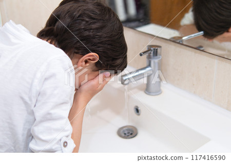 A boy washing his face under running tap 117416590
