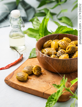 A green grill olives in wooden bowl on a light background with olive oil and basil. A green grill olives in wooden bowl on a light background with olive oil and basil. 117416832