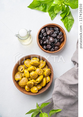 A set of green grill and black dried olives in wooden bowls on a light background with olive oil A set of green grill and black dried olives in wooden bowls on a light background with olive oil 117416850