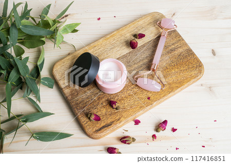 Face cream and massager on a wooden table. The concept of care cosmetics with rose and eucalyptus 117416851