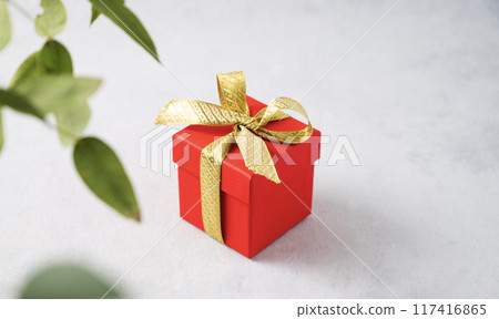 A red gift box with a gold ribbon on a gray background with branch flower. A red gift box with a gold ribbon on a gray background with branch flower. 117416865