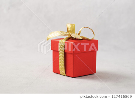 A red gift box with a gold ribbon on a gray background. The concept of holiday photography A red gift box with a gold ribbon on a gray background. The concept of holiday photography 117416869