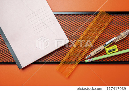 A ruler, pencil, and pen are on a table next to a notebook 117417089