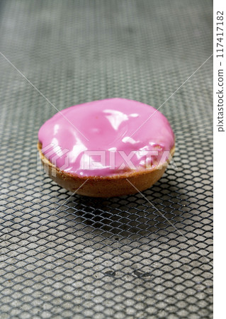 A pink frosted mini doughnut sits on a metal surface A pink frosted mini doughnut sits on a metal surface 117417182