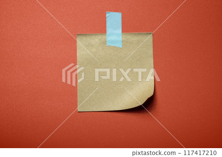 A piece of paper with a blue tape on it is stuck to a red surface A piece of paper with a blue tape on it is stuck to a red surface 117417210