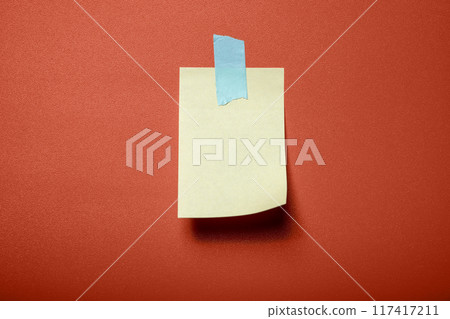 A yellow sticky note is stuck to a red background A yellow sticky note is stuck to a red background 117417211