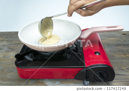 A person is cooking food in a pan on a stove A person is cooking food in a pan on a stove 117417249