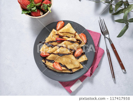 Sweet crepes with fresh strawberry and chocolate  on a gray plate on a light background.  117417938