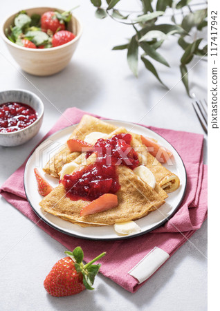 Sweet pancakes with berry jam, fresh strawberries and banana on a light background.  117417942