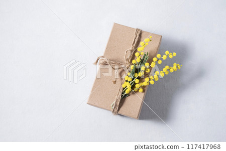 Gift craft box with yellow mimosa flowers on a light background. The concept for the spring holiday Gift craft box with yellow mimosa flowers on a light background. The concept for the spring holiday 117417968