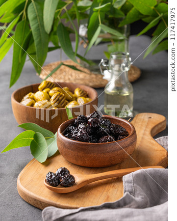 A set of green and black dried olives in bowls on a wooden cutting board on a dark background  117417975