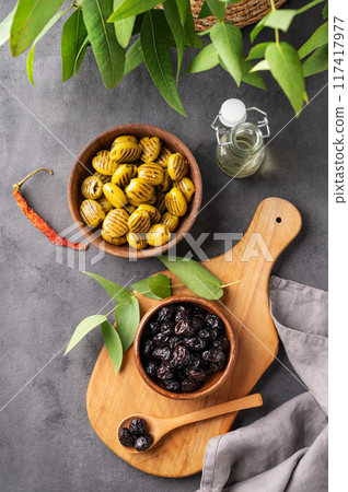 A set of green and black dried olives in bowls on a wooden cutting board on a dark background A set of green and black dried olives in bowls on a wooden cutting board on a dark background 117417977