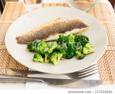 Fried fillet of sea bass with garnish of broccoli on black warm stone plate 117418680