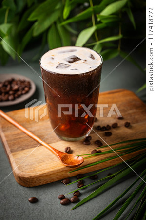 Iced coffee brew in a glass on a wooden board on a green background with coffee beans Iced coffee brew in a glass on a wooden board on a green background with coffee beans 117418772