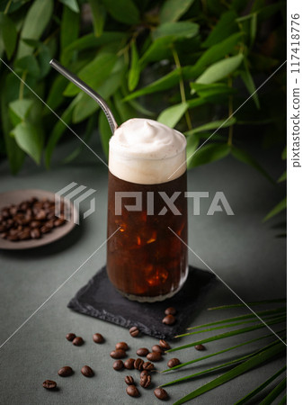 Iced coffee brew with foam in a glass on a black board on a dark green background with coffee beans Iced coffee brew with foam in a glass on a black board on a dark green background with coffee beans 117418776