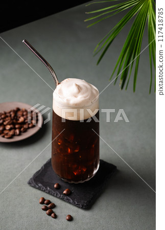Iced coffee brew with foam in a glass on a black board on a dark green background with coffee beans Iced coffee brew with foam in a glass on a black board on a dark green background with coffee beans 117418785