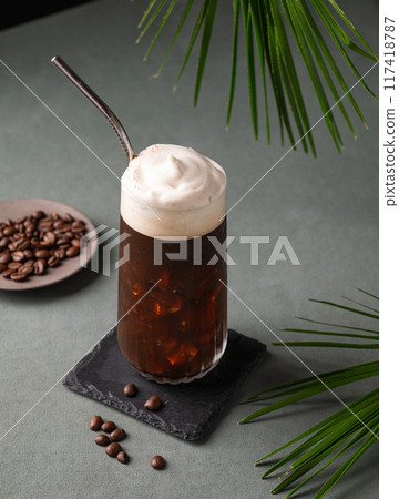 Iced coffee brew with foam in a glass on a black board on a dark green background with coffee beans Iced coffee brew with foam in a glass on a black board on a dark green background with coffee beans 117418787
