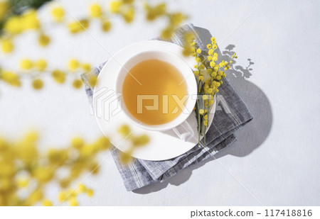 A spring bouquet with yellow mimosa flowers over a cup of herbal tea on a white table.  117418816