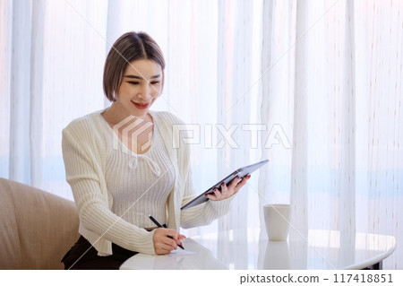 A woman is sitting at a table with a tablet and a pen 117418851