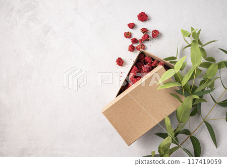 Craft box with red dry flowers on a gray textured background with branch plant.  117419059