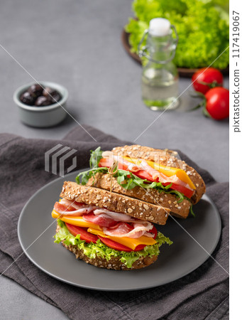 Club sandwich on a plate with a bacon, cheese, tomato and lettuce on a dark background Club sandwich on a plate with a bacon, cheese, tomato and lettuce on a dark background 117419067