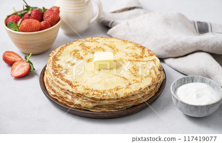 Sweet pancakes stacked with butter, sour cream and fresh strawberries on a light background. Sweet pancakes stacked with butter, sour cream and fresh strawberries on a light background. 117419077