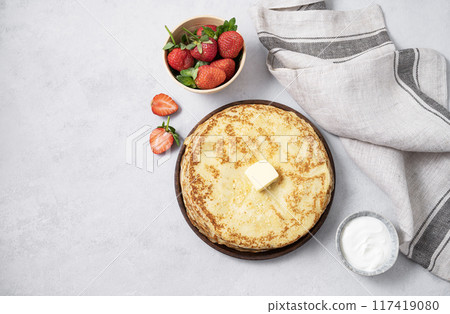 Sweet pancakes stacked with butter, sour cream and fresh strawberries on a light background. 117419080