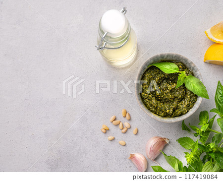 Traditional Italian pesto in a bowl with green basil, pine nuts and olive oil on a light background. 117419084