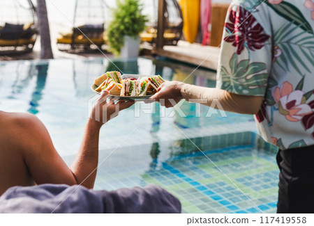 Waiter serving club sandwich at lunch by the swimming pool. 117419558