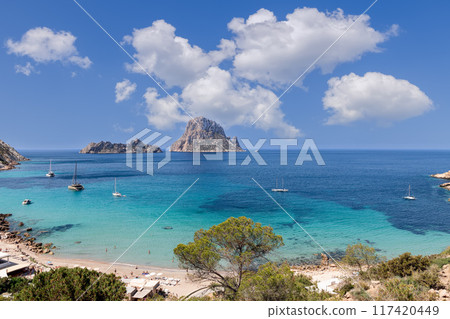 Cala Hort in Ibiza with Es Vedra island, turquoise waters, anchored yachts, puffy clouds 117420449