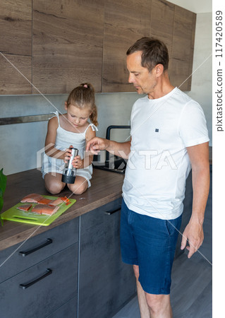 Young father and daughter cooking fish together in home kitchen Young father and daughter cooking fish together in home kitchen 117420589